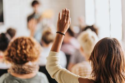 Pictured: A woman in a small audience raising her hand