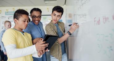 Students doing math on a whiteboard with their teacher
