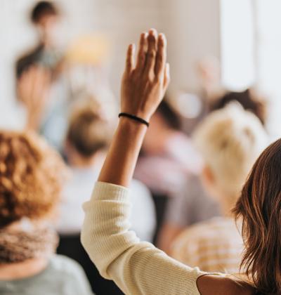 Pictured: A woman in a small audience raising her hand