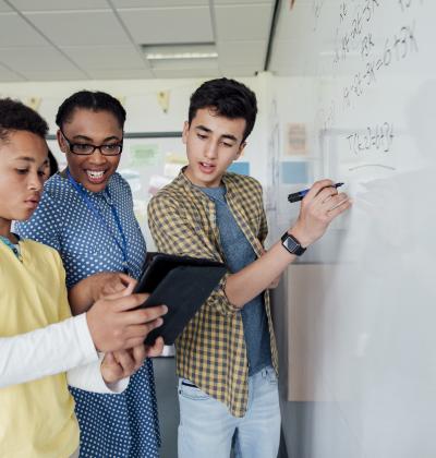 Students doing math on a whiteboard with their teacher