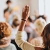 Pictured: A woman in a small audience raising her hand